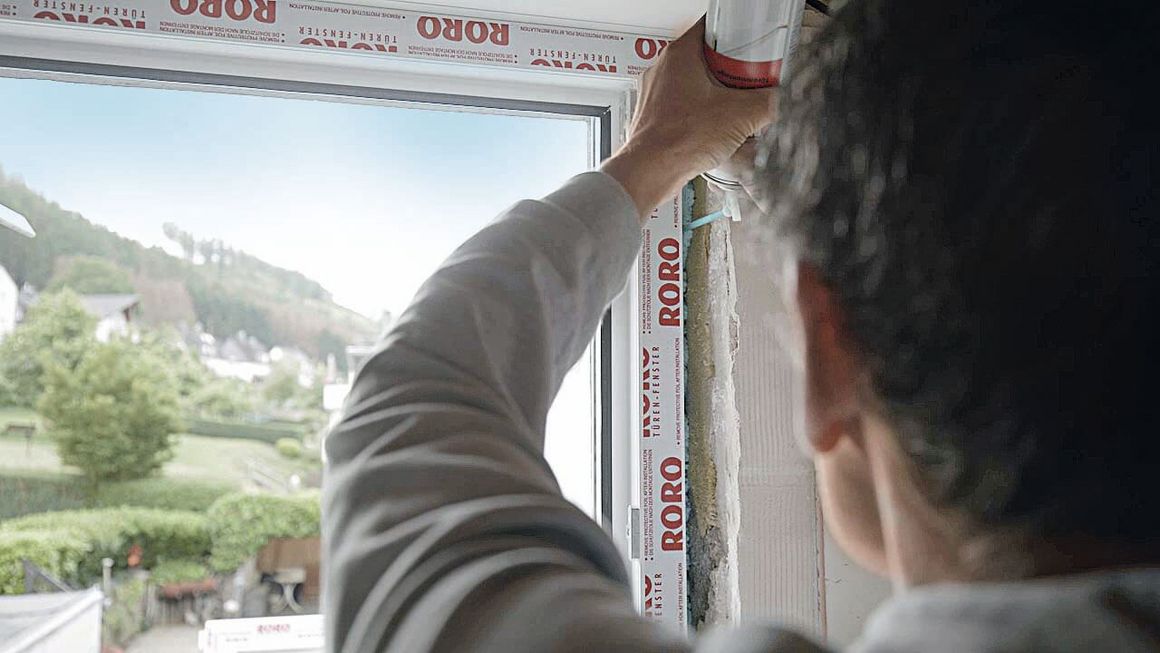 Ein Mann beim Abdichten eines neu eingebauten Fensters.